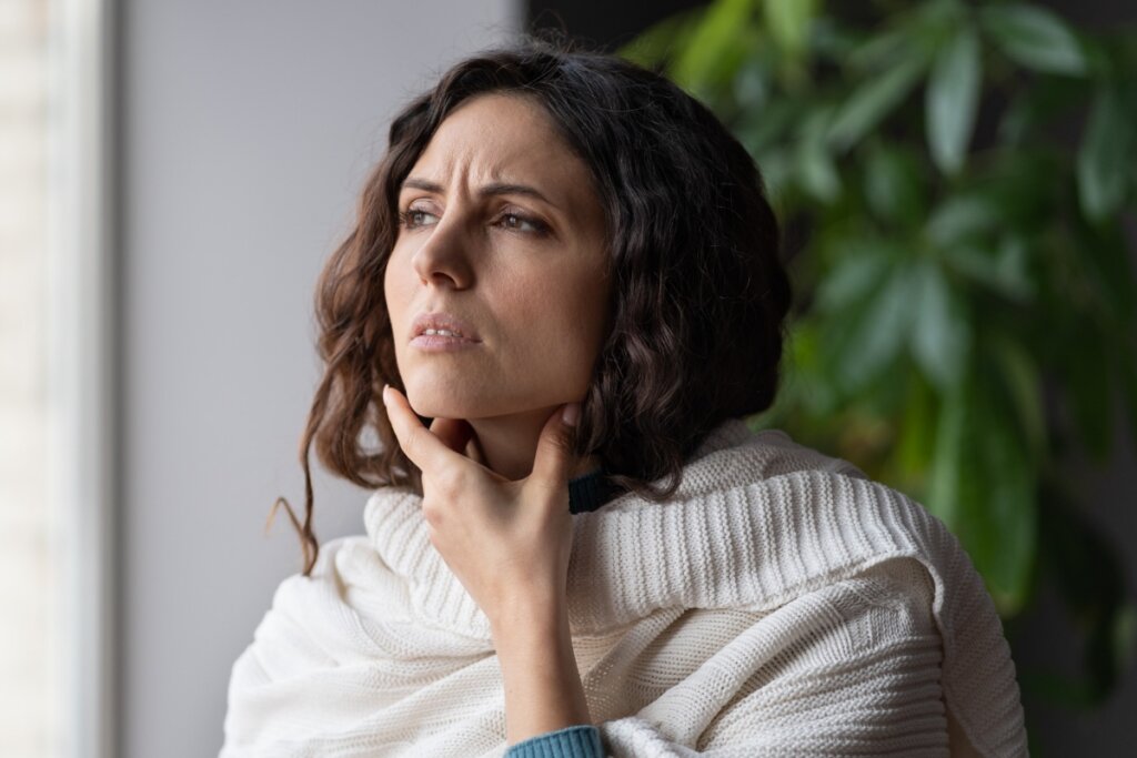 Mulher com a mão na garganta em frente a uma janela