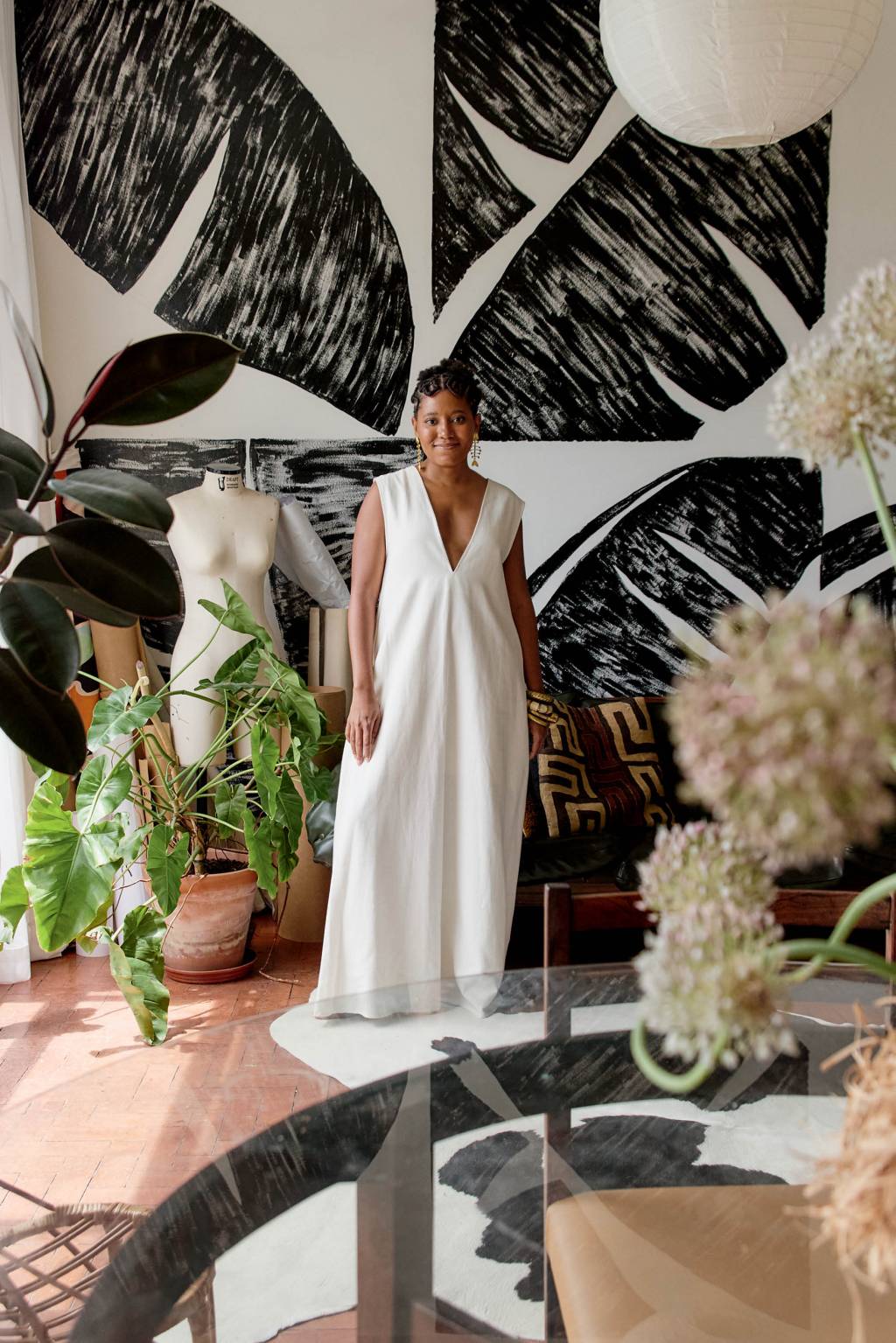 mulher de vestido branco em pé em frente à parede com estampa de folha de bananeira