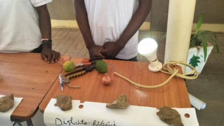 Perante as flutuações de energia que o impediam de estudar, um aluno do 11.º ano decidiu usar o que aprendeu na escola e gerar eletricidade, recorrendo a limão e cebola. Imagem mostra duas pessoas atrás de uma mesa com a experiência a dar luz a uma lâmpada