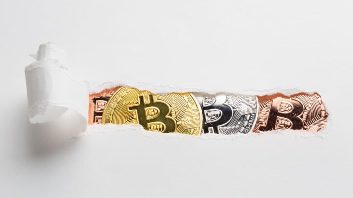 Uma folha de papel, rasgada no centro, a mostrar moedas de Bitcoin