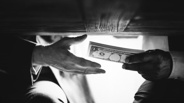 Duas mãos a passarem dinheiro debaixo de uma mesa