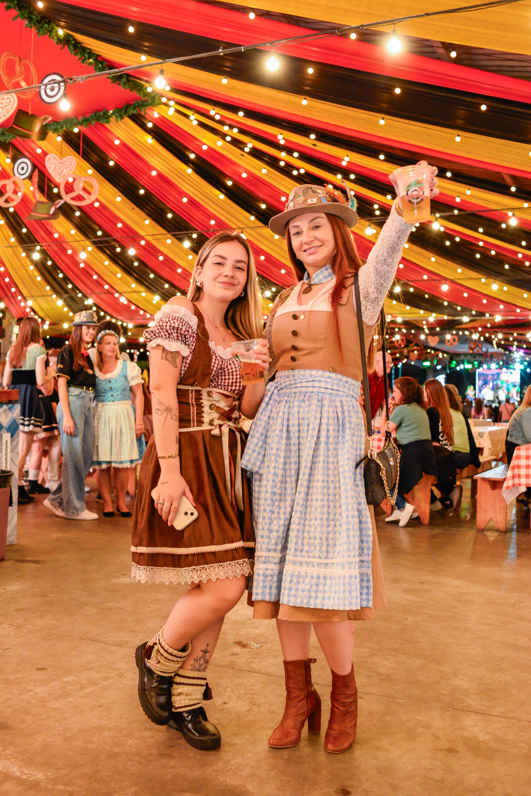 Duas mulheres com trajes típicos da Schützenfest brindam sob tenda decorada
