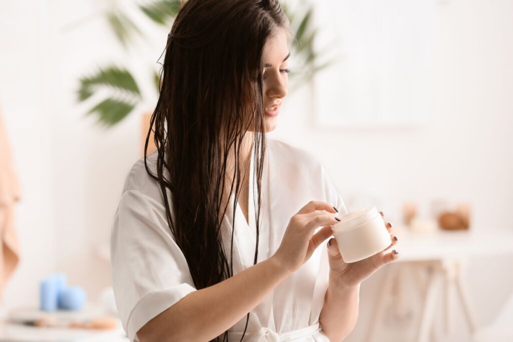 Mulher com o cabelo liso longo, cuidando do cabelo após o banho, usando um roupão branco