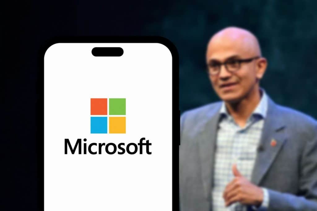 Satya Nadella ao lado de um smartphone exibindo o logo da Microsoft em sua tela