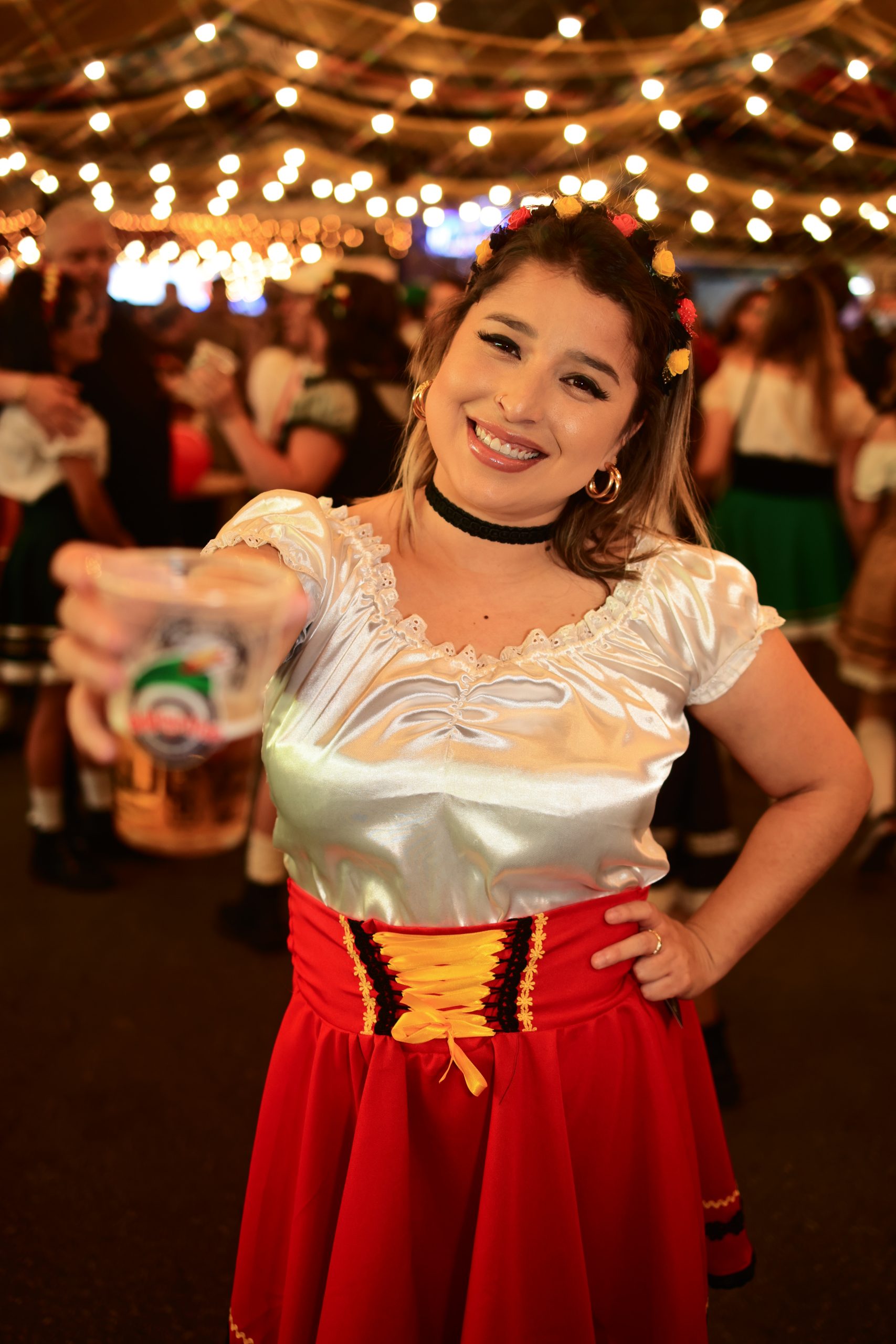 Mulher com trajes típicos oferece chope com sorriso durante a festa