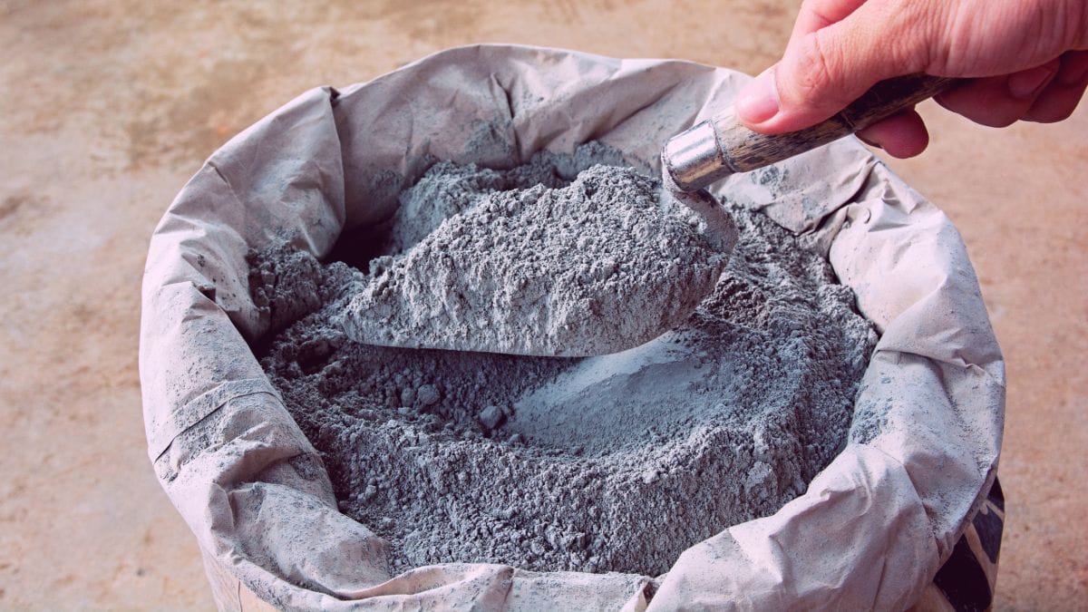 pessoa pegando um pouco de cimento de um saco com um pá de construção civil