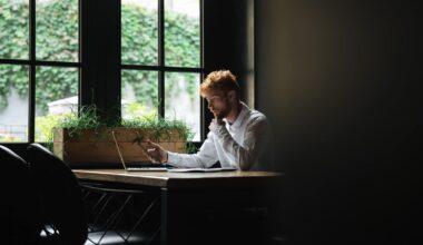 Trabalhador, no canto de uma sala, à janela, com um computador e um smartphone