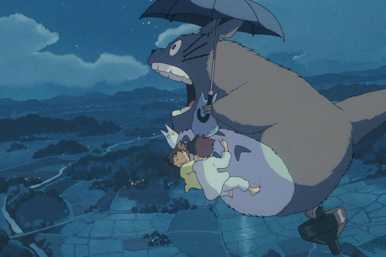 Totoro, criatura grande e cinza, voa segurando um guarda-chuva aberto à noite. Três crianças estão penduradas em seu corpo enquanto sobrevoam uma paisagem rural iluminada por luzes distantes.