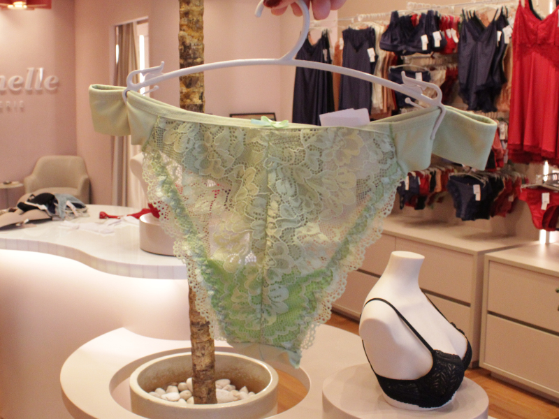 Calcinha de renda verde-água com cós de tecido liso, apresentada em um ambiente de loja elegante.