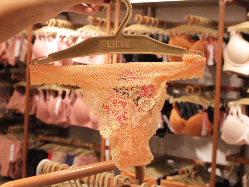 Calcinha de renda na cor laranja claro, destacando o padrão floral e o cabide da marca Liebe.