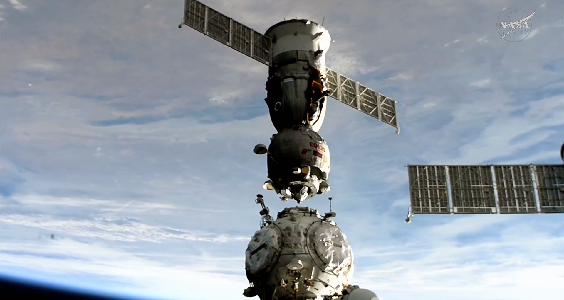 Um ônibus espacial se separa de sua porta de ancoragem em uma estação espacial com a Terra abaixo em um fundo azul e branco.