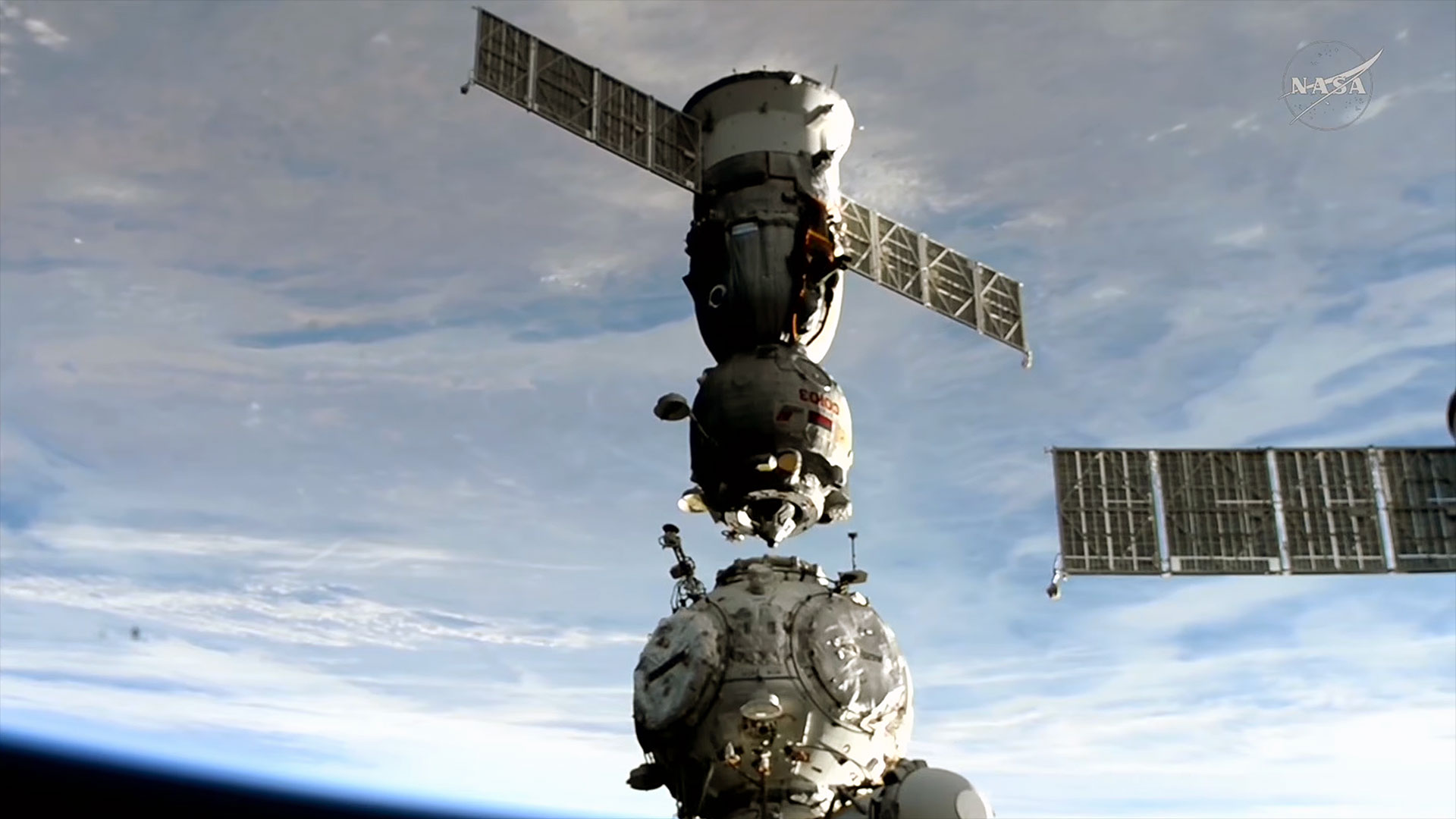 Um ônibus espacial se separa de sua porta de ancoragem em uma estação espacial com a Terra abaixo em um fundo azul e branco.