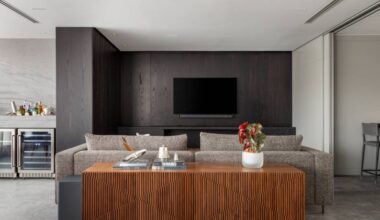 Elegância sóbria: tons de cinza e painéis de madeira ebanizada marcam apê