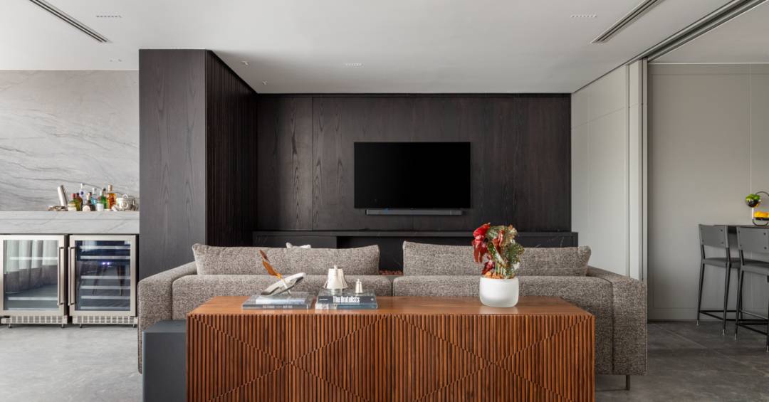 Elegância sóbria: tons de cinza e painéis de madeira ebanizada marcam apê