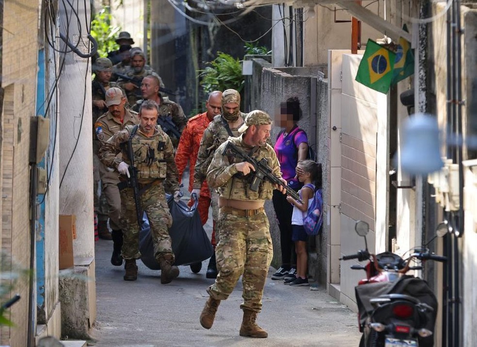 Mulher cobre o rosto de criança durante a passagem de policiais com o corpo de suspeito morto em operação na Ladeira dos Tabajaras — Foto: Márcia Foletto / Agência O Globo