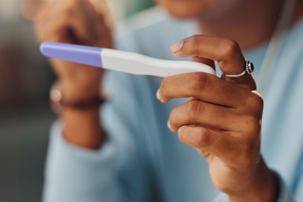 Mão segurando um teste de gravidez branco e azul