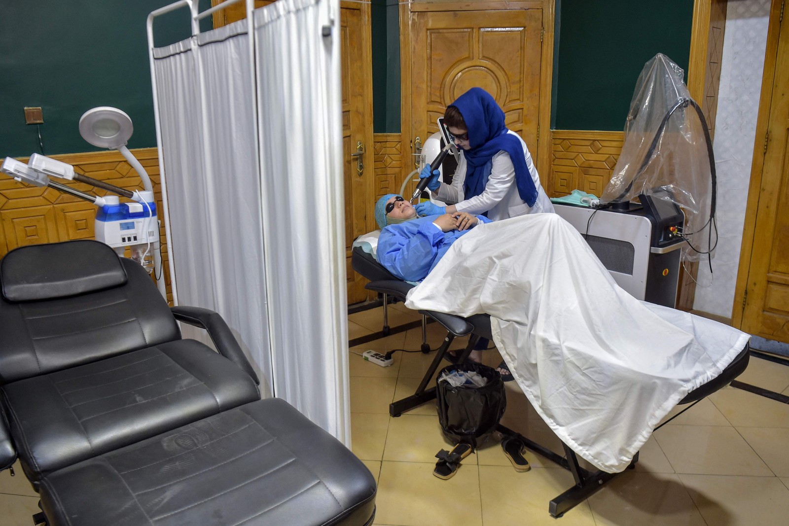 Equipe médica realiza tratamento a laser no rosto de uma mulher afegã em uma clínica de estética em Cabul — Foto: Wakil KOHSAR / AFP