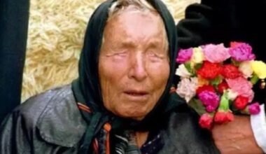 Retrato de Baba Vanga, mulher idosa com lenço na cabeça e olhos fechados, segurando flores coloridas.