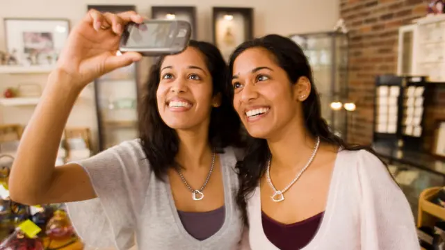 Duas gêmeas idênticas sorriem enquanto tiram uma selfie juntas
