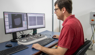 Imagem: Homem branco de camisa vermelha sentado em frente a um computador com dois monitores (Foto: Gutierrez Réges)