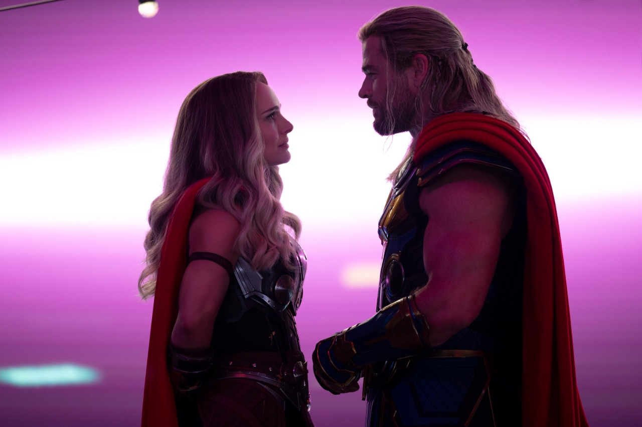 Cena de Jane (Natalie Portman) e Thor (Chris Hemsworth) olhando um para o outro em cenário de filme com iluminação rosa e roxa