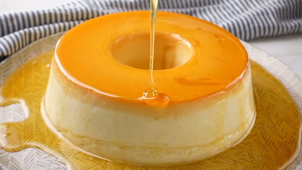 Pudim de iogurte inteiro com calda brilhante sendo despejada no centro da sobremesa