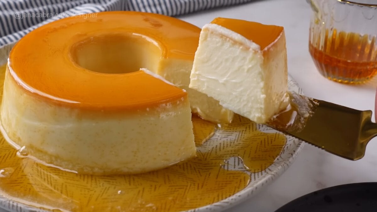 Fatia de pudim de iogurte sendo retirada com espátula, mostrando interior cremoso