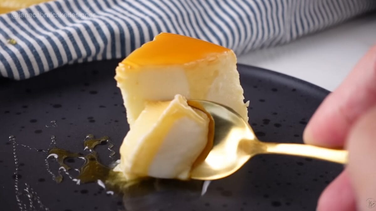 Fatia de pudim de iogurte sendo retirada com espátula, mostrando interior cremoso