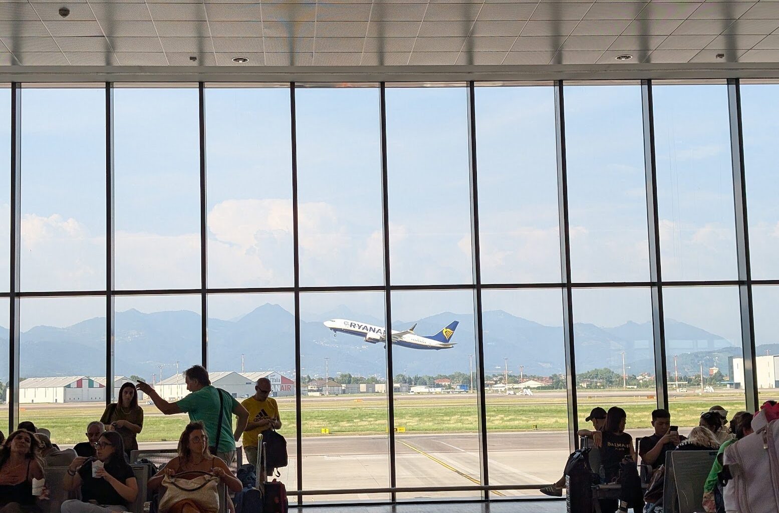 Avion Ryanair în zbor văzut din aeroport. Pasageri așteptând zborul care să-i ducă acasă.