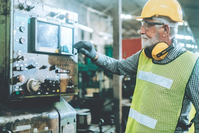 Un bătrân reglează un utilaj la locul de muncă