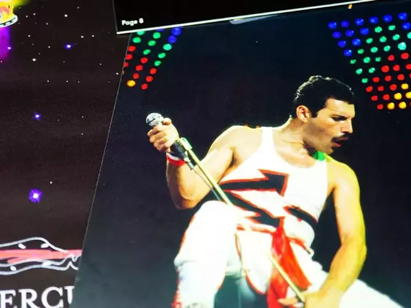 Imagine de arhiva cu starul Queen, Freddie Mercury, in timpul unui concerc, imbracat in alb, cu microfonul in maini, pe un findal negru cu lumini colorate