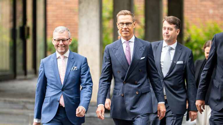 Alexander Stubb i en randig kostym går bredvid män och kvinnor på en gata.