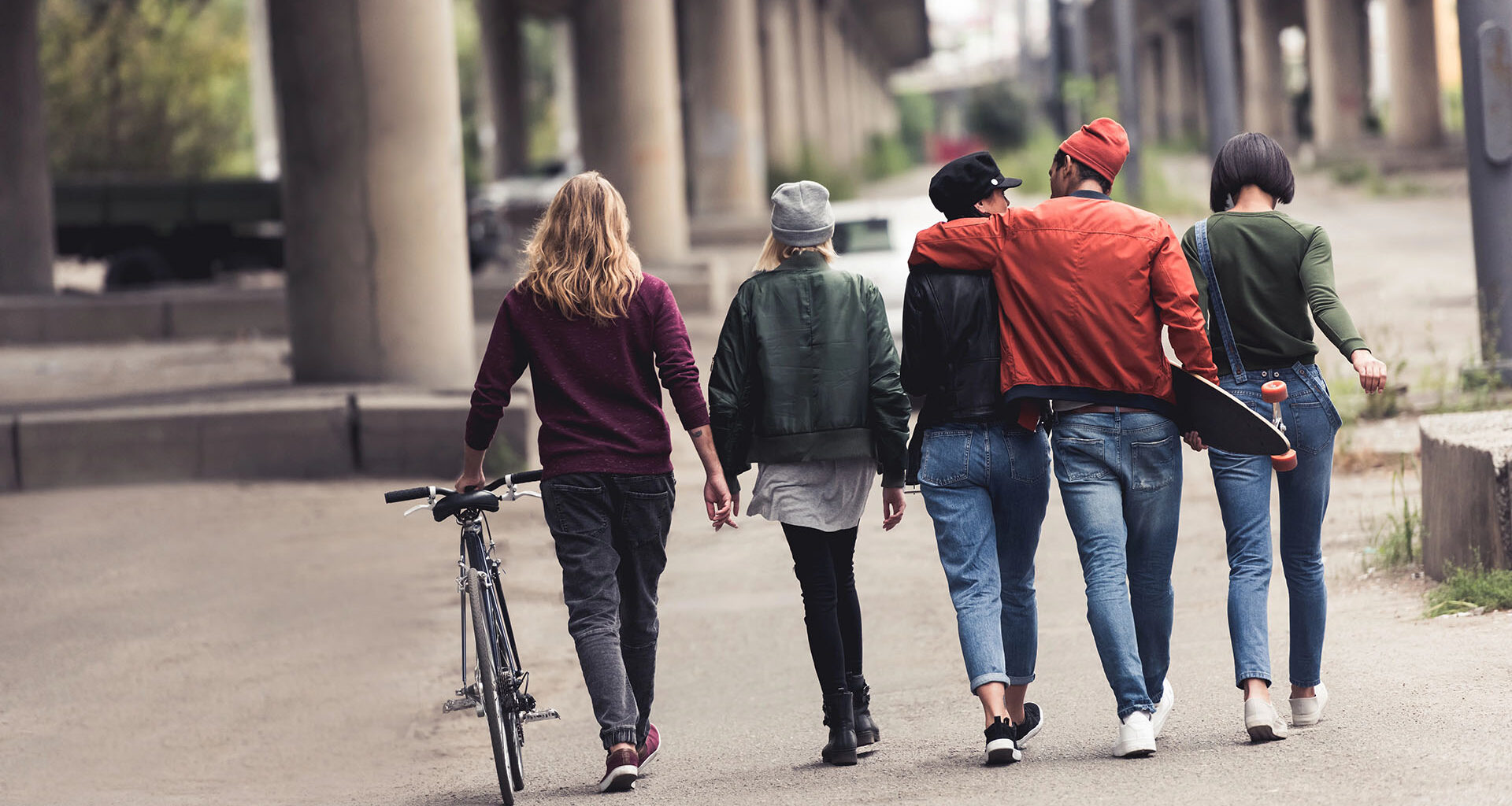 Fem yngre personer går på rad under en bro.