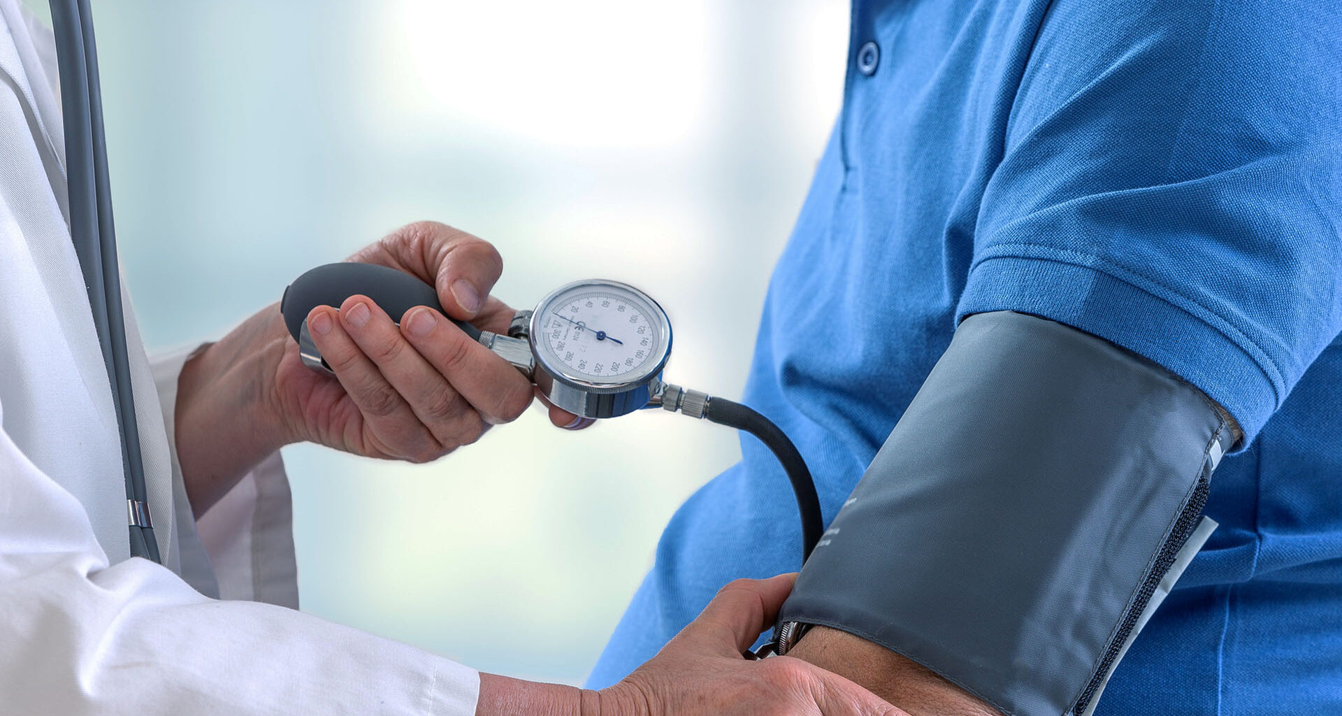 Läkare mäter blodtrycket på en patient i blå tröja.