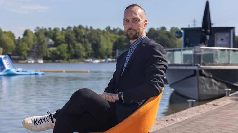 En man i kaval sitter i en fåtölj på en brygga. 