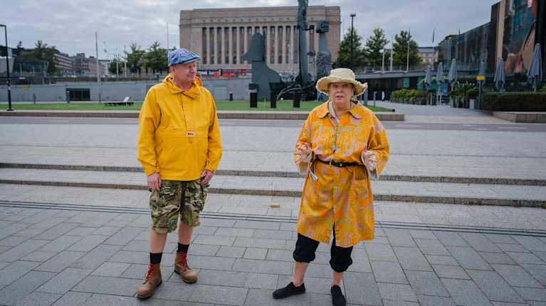Två personer i gula rockar står på Medborgartorget i Helsingfors. 