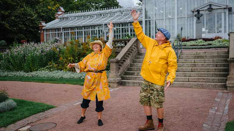 Två personer i gula rockar dansar framför Vinterträdgården i Helsingfors. 
