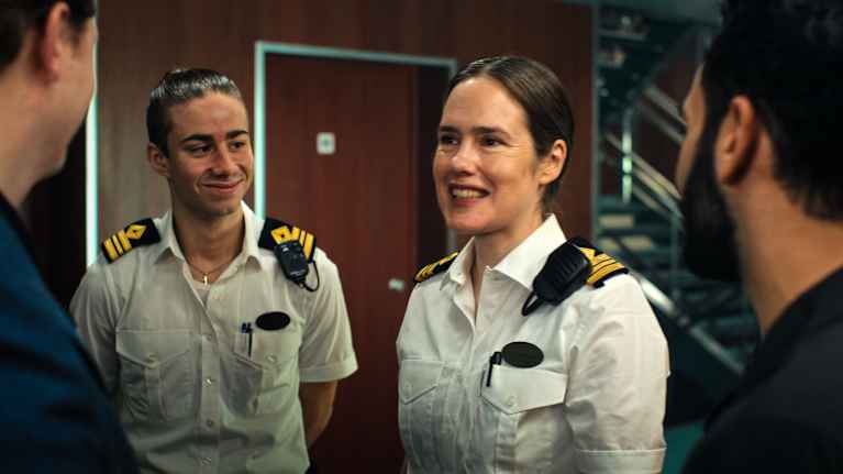 Två av fartygets säkerhetsvakter ler då de pratar med två passagerare. Vakterna har vita skjortor med epåletter och radiotelefoner.