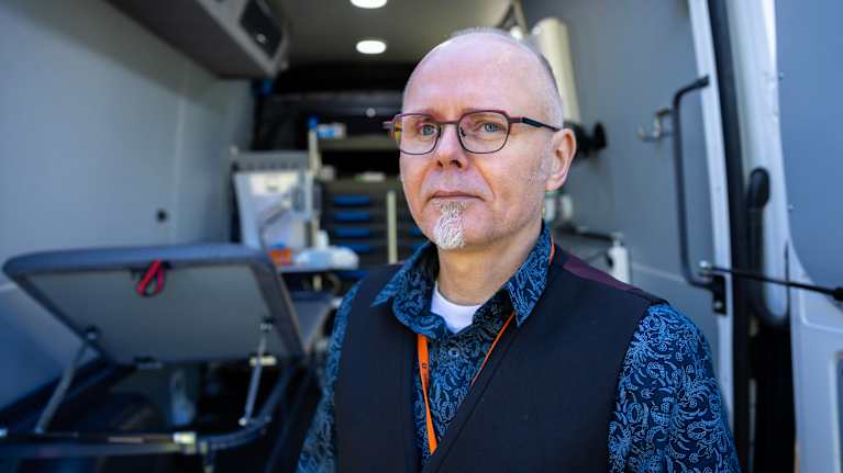 En man i skjorta och väst som står i en mobil enhet utrustad med medicinsk utrustning.