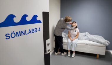 Person sätter någonting runt huvudet på en testdeltagare som sitter på säng.