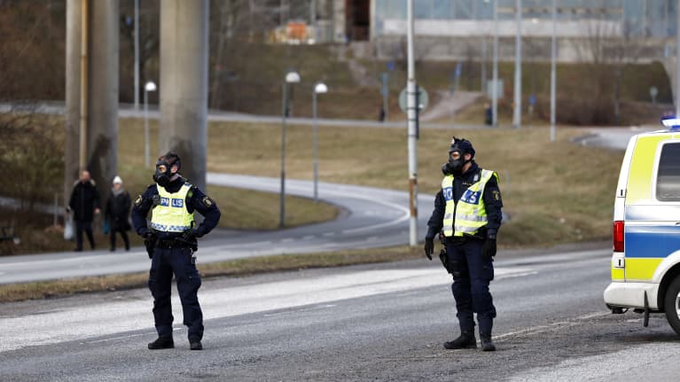 Två poliser med skyddsmask på spärrar av en väg.
