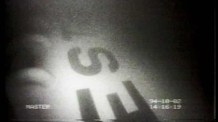 En suddig svartvit bild av Estonias vrak under vatten. Bokstäverna EST går att läsa på skrovet.