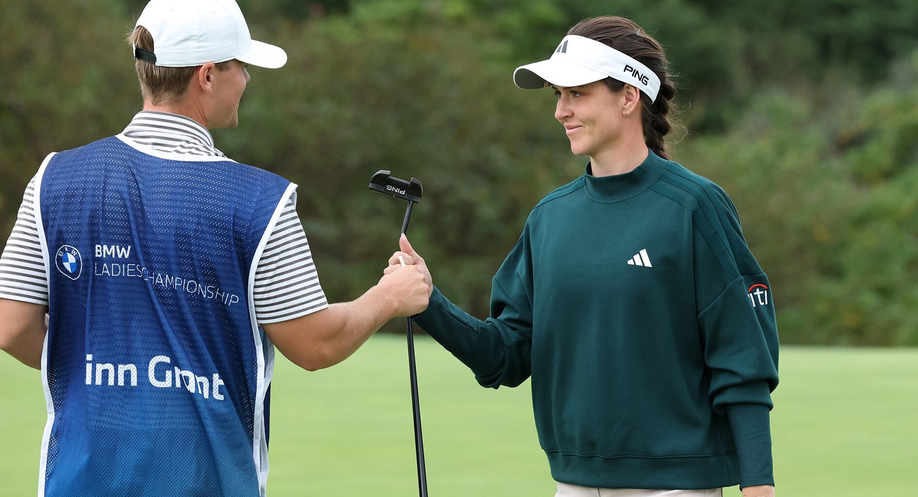 golfspelaren linn grant iklädd grön golftröja ger sin putter till caddien