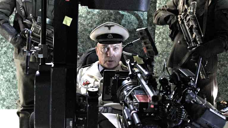 Skådespelare är klädda i militäruniformer från andra världskriget och omgivna av filmutrustning som kameror och mikrofoner.