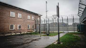 Fängelsegården är omgärdad av höga stängsel och taggtråd. Inne på gården finns en basketkorg samt bänkar längs väggen av byggnaden.
