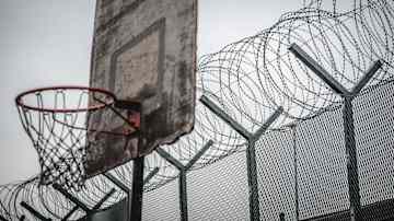 En sliten basketkorg framför ett högt stängsel med taggtråd.