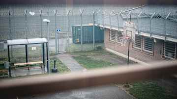 Bilden visar en utsikt från ett fönster mot en gård omgiven av höga staket med taggtråd.