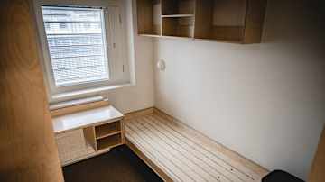 En cell med en brits av trä och ett skrivbord.