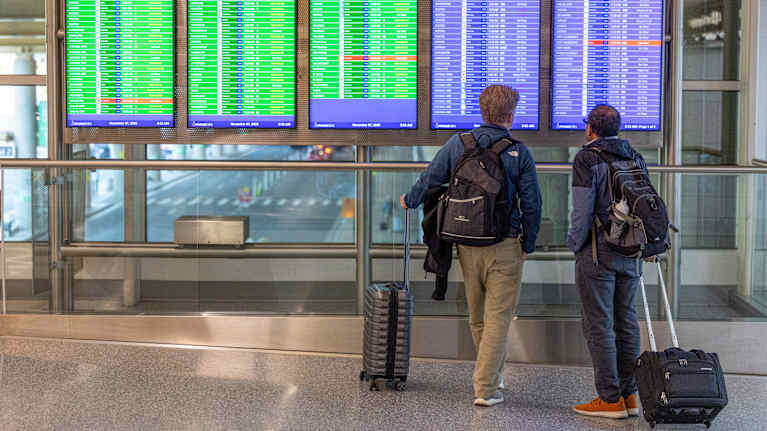 Två resenärer studerar avgångstavlor på en flygplats för att kontrollera sina flyg.