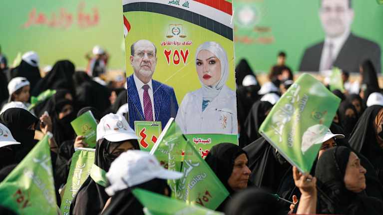 Kvinnor i Irak håller upp kampanjafficher och flaggor för shiamuslimska kandidaten Nouri al-Maliki i valet 2025.